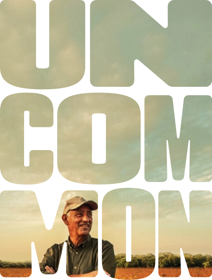 The word 'UNCOMMON' is displayed in large bold letters, each filled with a scenic landscape of a field, trees, and a clear sky. Inside the letter 'O,' a person wearing a hat stands with arms crossed, blending into the natural backdrop.